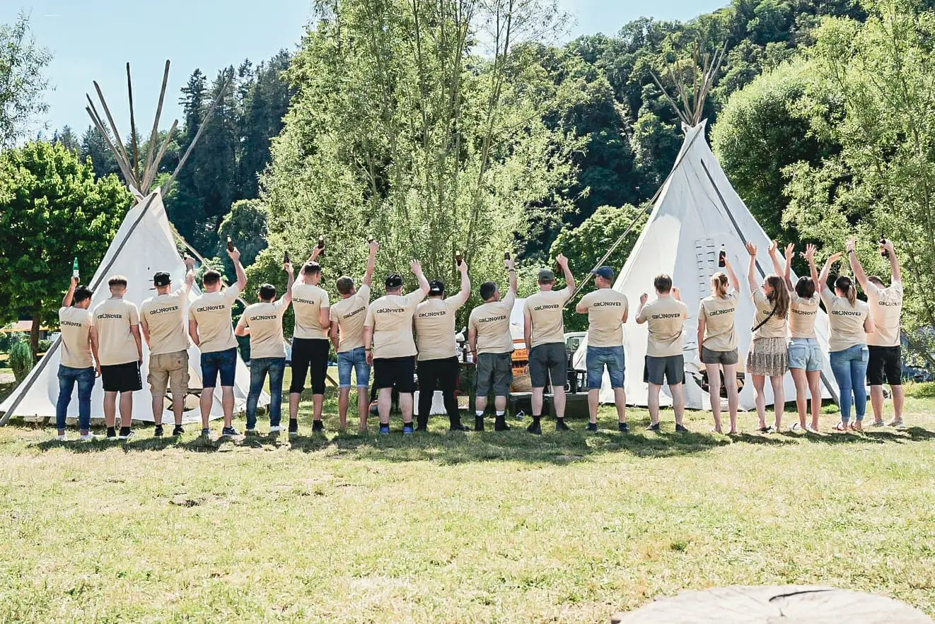 Die Gronover Gruppe steht mit dem Rücken zur Kamera und hebt jubelnd ihre Getränke in die Höhe